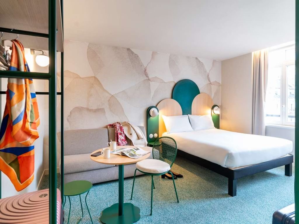 Chambre d’hôtel rénovée, tête de lit verte et papier peint minéral